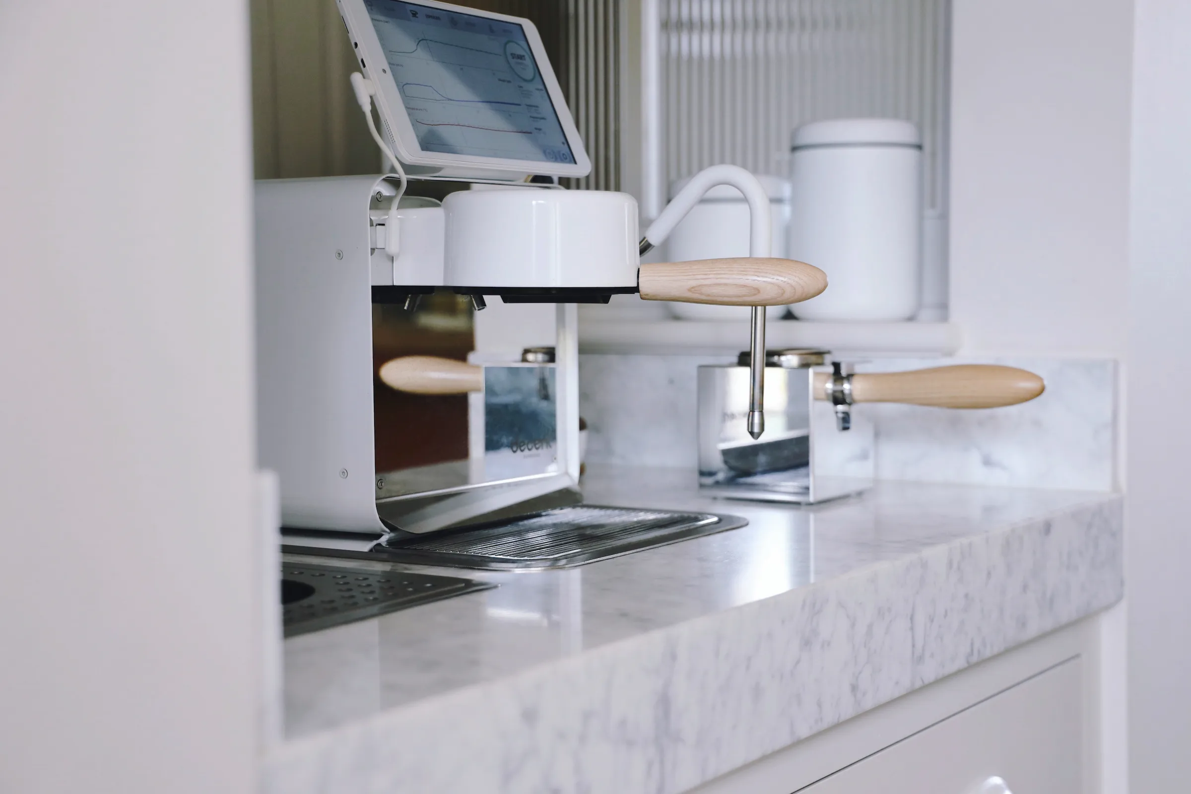 Modern espresso machine with tablet display on white marble counter, chrome portafilter and steam wand